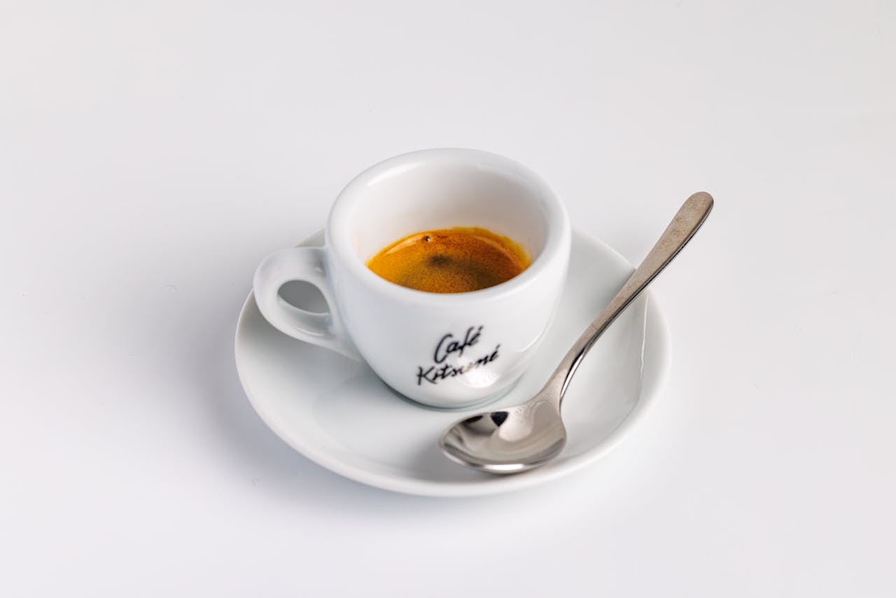 Minimalist shot of espresso in branded cup with spoon on saucer.