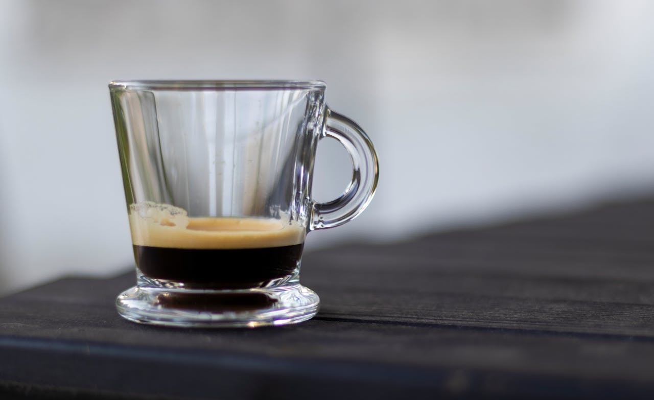 A close-up shot of a rich espresso in a clear glass cup on a dark table.